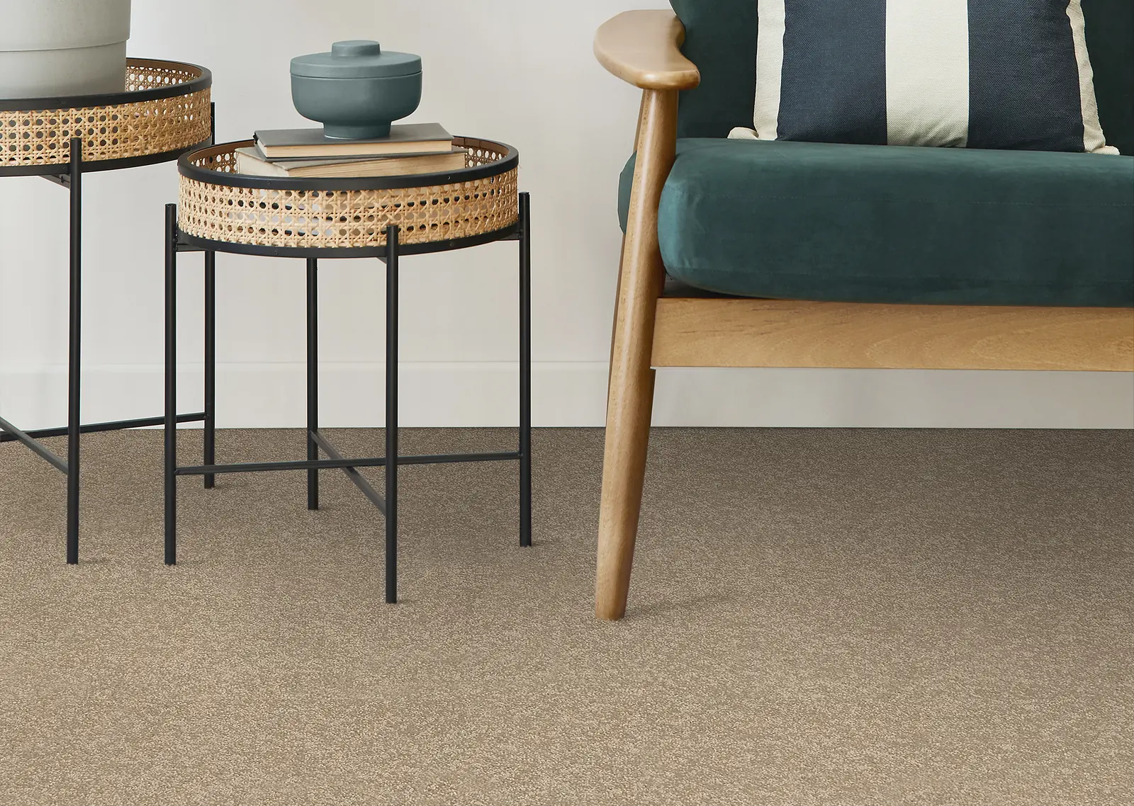 Warm oatmeal carpet under a green velvet chair and two rattan side tables