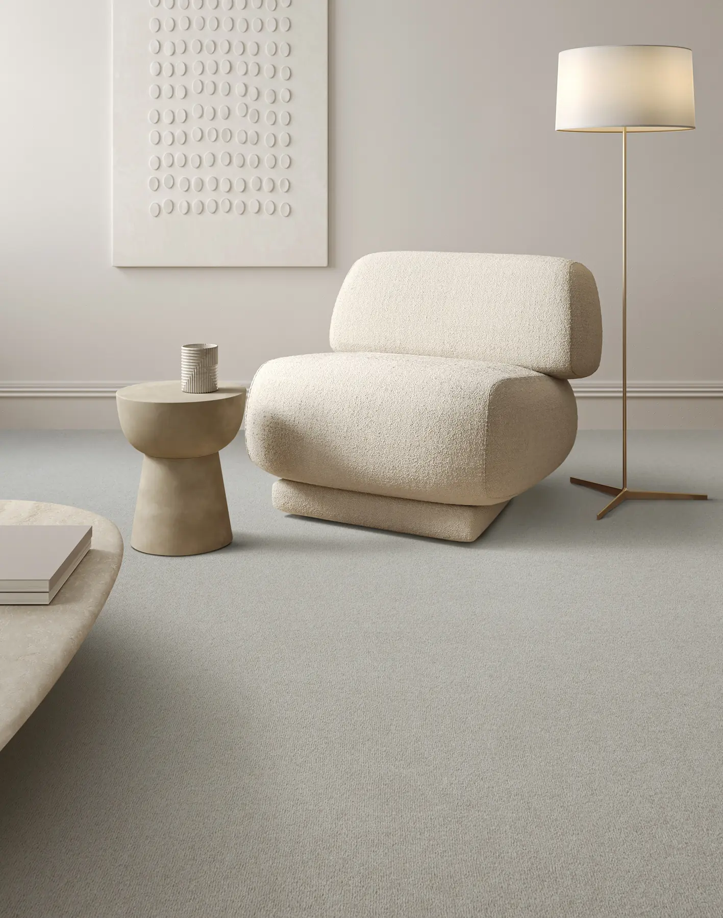Pale grey carpet with a cream bouclé chair, a floor lamp and a stone side table